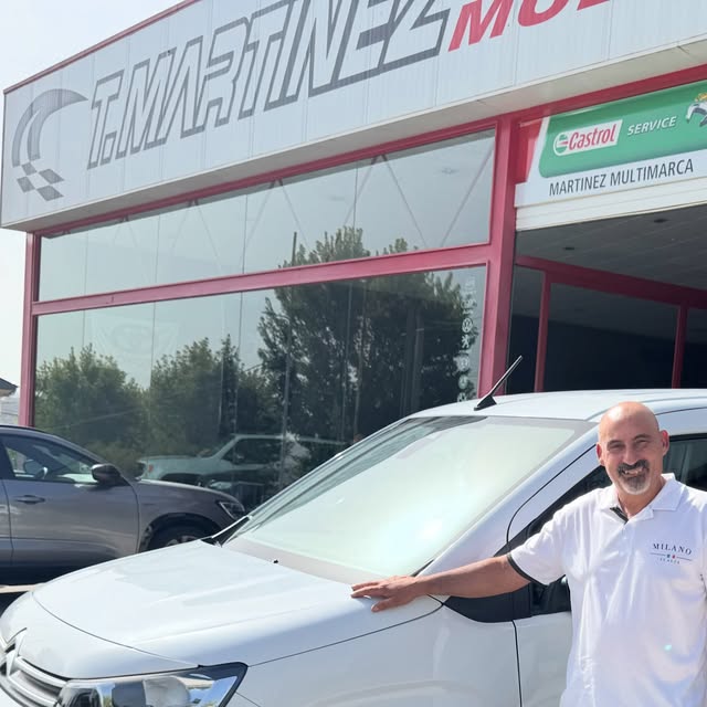 Citroën Berlingo blanca frente al concesionario, con un hombre sonriente apoyado en ella
